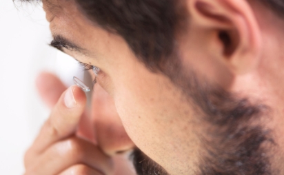 A close-up shot of a man applying a contact lens to left eye